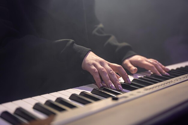 Female hands play piano keys in a dark hazy room