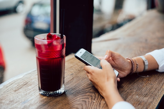 Free photo female hands typing a message on mobile phone, sitting for the table with fruit cocktail