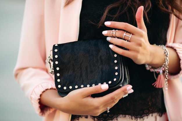 Female hands with beautiful nail polish and rings holding small black bag.