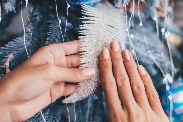 Female hands with Christmas new year nail design. Nude beige nail polish manicure, one finger shiny golden bronze