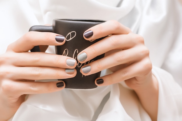 Free photo female hands with glitter nail design holding black cup.