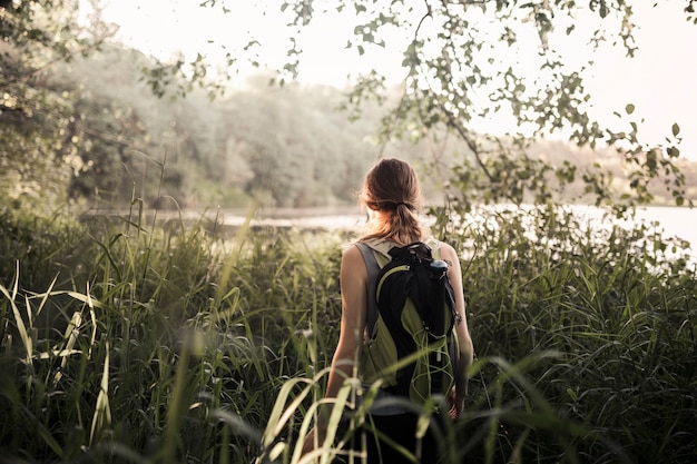 Free photo female hiker walking in the green grass near the lake