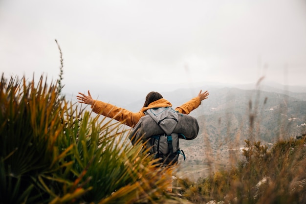 A female hiker with backpack outstretching her arms in mountains