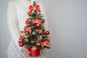 Free photo female holding a christmas tree decorated with red ornaments