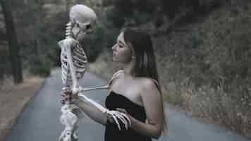 Free photo female holding decorative skeleton of man standing on road