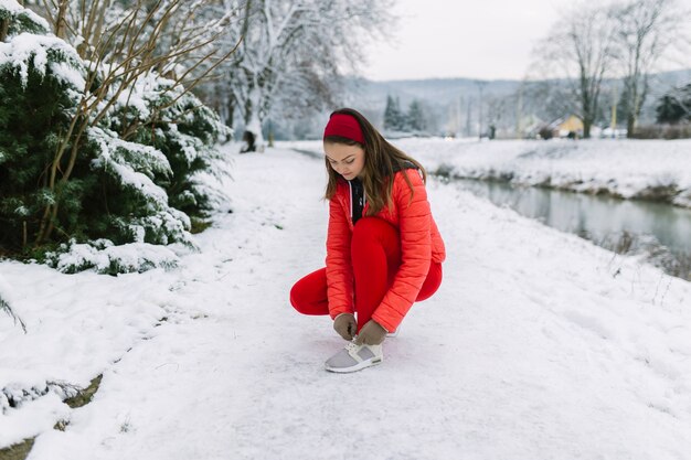 Female jogger tying shoelace near the lake in winter