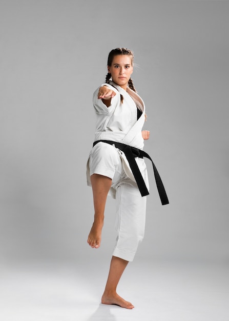 Female karate fighter performing kick isolated on grey background