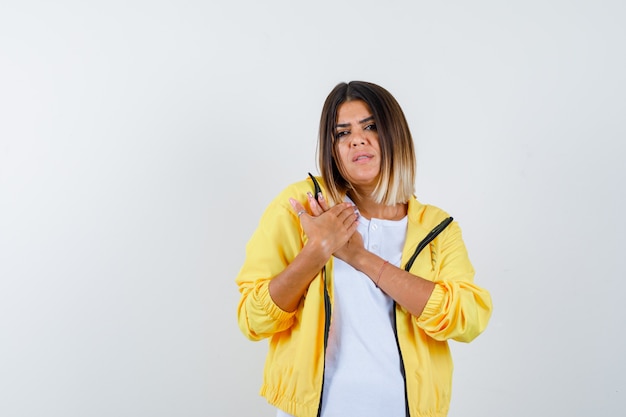 Female keeping hands on chest in t-shirt, jacket and looking sad , front view.