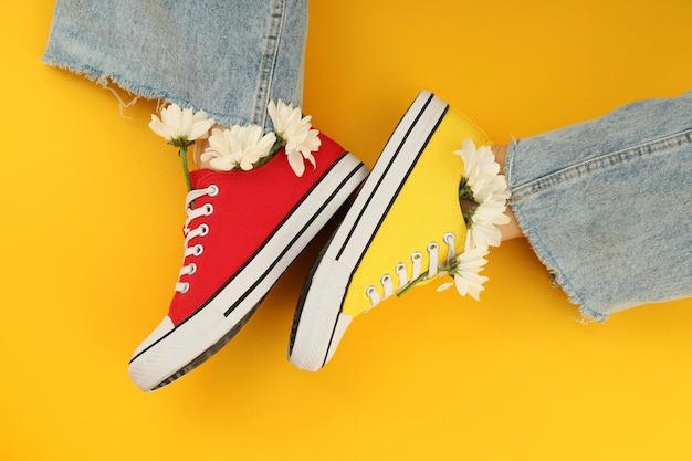 Female legs in sneakers with flowers on yellow background