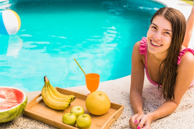 Free photo female lying on edge of pool with fruits