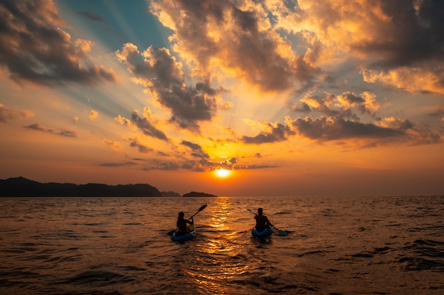 Free Photo female and a male sailing with canoes close to each other at sunset