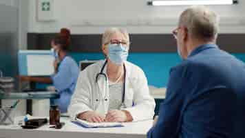 Free photo female medic consulting retired sick patient in medical cabinet, attending examination appointment at health care center. checkup visit consultation with diagnosis treatment during pandemic.