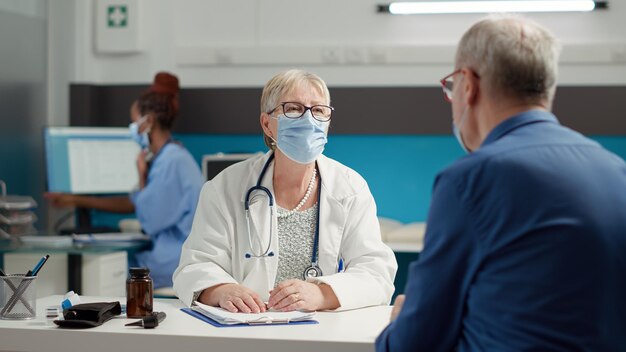 Female medic consulting retired sick patient in medical cabinet, attending examination appointment at health care center. Checkup visit consultation with diagnosis treatment during pandemic.