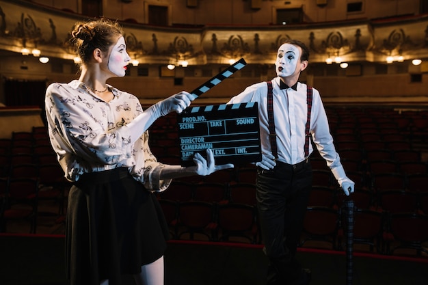 Free photo female mime artist holding clapper in front of male mime artist performing on stage