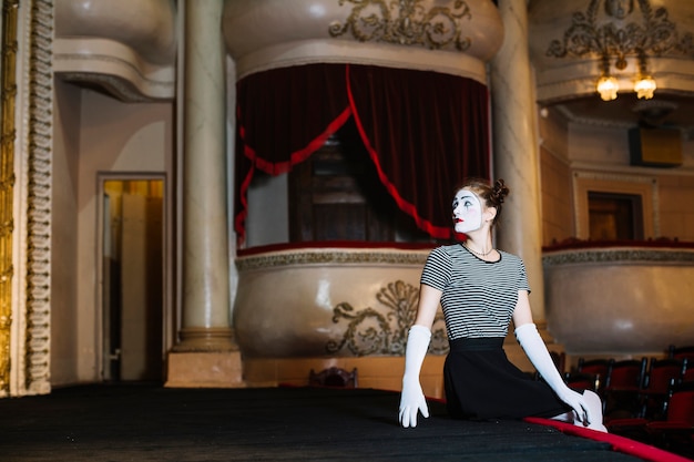 Free photo female mime artist sitting on the edge of stage in the auditorium