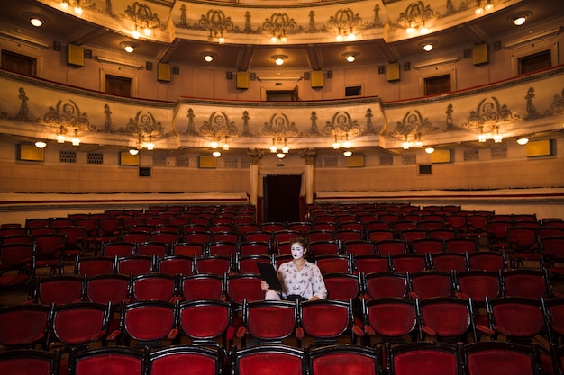 Free photo female mime with manuscript sitting at the center of auditorium