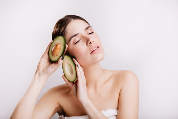 Female model with clear skin inspired posing on isolated wall with nutritious wholesome avocados.