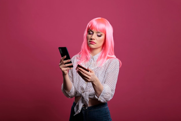 Free Photo female model with pink hair using credit or debit card and smartphone for online shopping clothes purchase. making money transaction to buy on internet website, using mobile phone retail app.