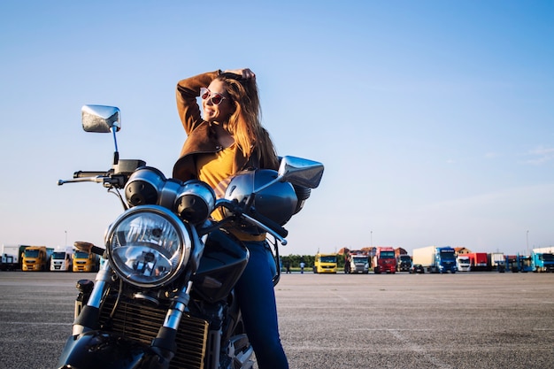 Female motorcyclist in leather jacket sitting on retro motorbike and smiling