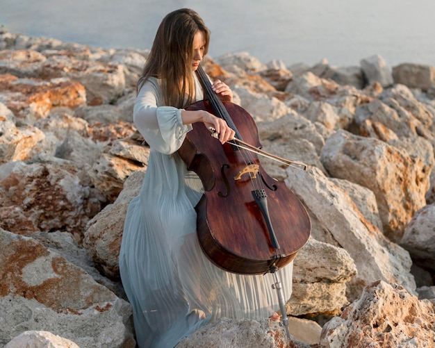 Free Photo female musician playing cello on rocks outdoors