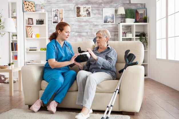 Female nurse showing elderly age woman how to use virtual reality glasses in nursing home.