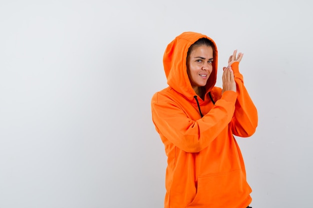 Female in orange hoodie posing while standing and looking alluring 