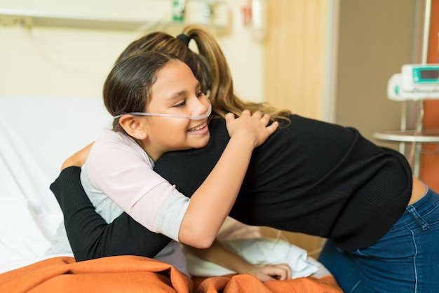 Female parent embracing sick daughter during treatment at hospital and smiling