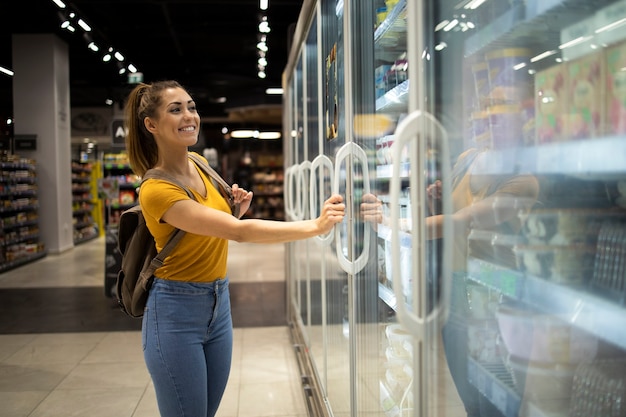 Free photo female person with shopping cart opening fridge to take food in grocery store