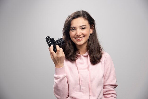 Female photographer smiling with camera on gray wall. 