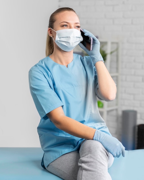 Female physiotherapist with medical mask talking on smartphone