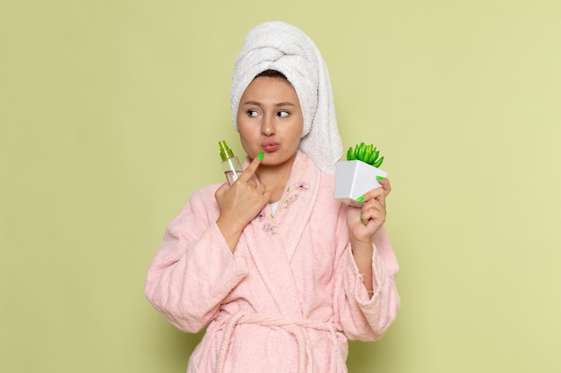 Free Photo female in pink bathrobe holding spray flask and plant