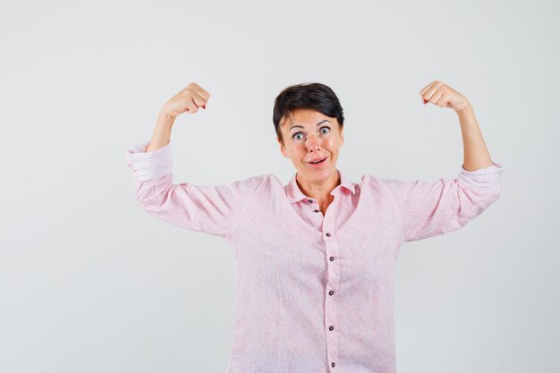 Female in pink shirt showing muscles of arms and looking powerful , front view.