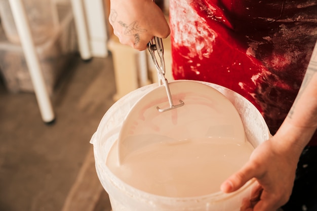 Female potter's hand inserting the plate in the paint bucket with tong