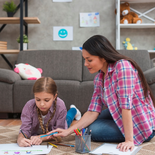 Female psychologist helping girl to draw the drawing on paper