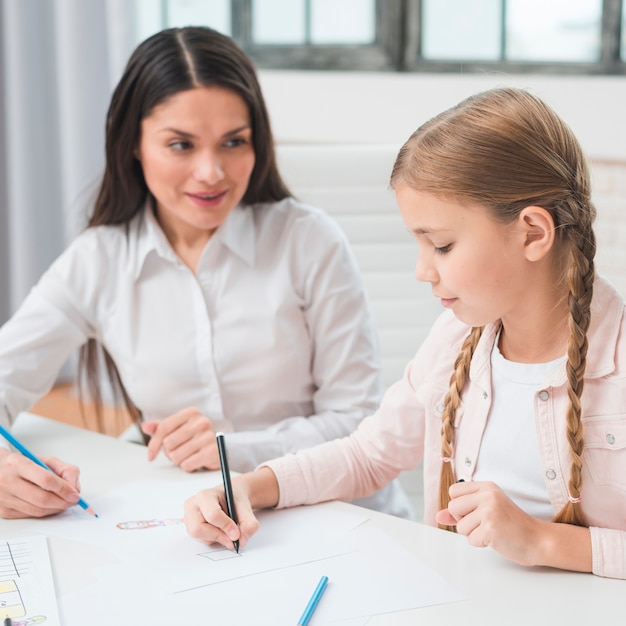 Female psychologist looking at girl drawing with colored pencil