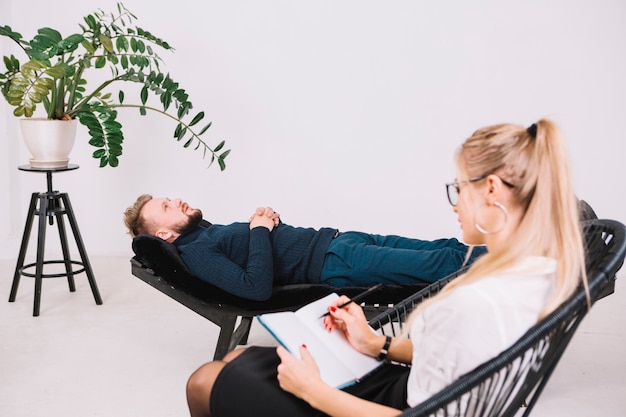 Free photo female psychologist writing notes on diary while patient lying on couch in clinic