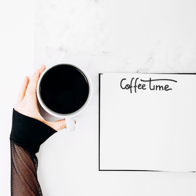 A female's hand holding coffee cup with handwritten text on notebook over the desk