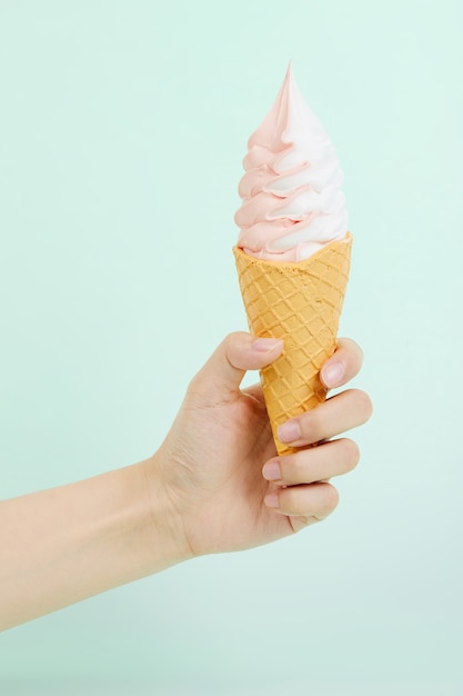 Free photo female's hand holding delicious soft ice cream in a crispy waffle cone on blue surface