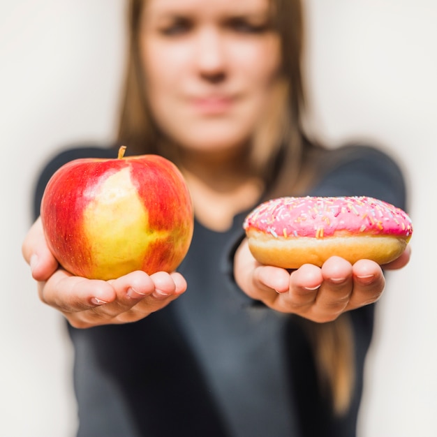 Female's hand holding fresh apple and donut