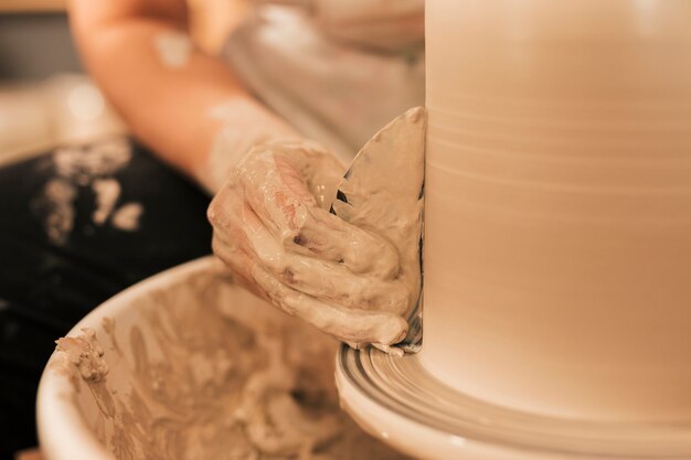 Female's hand smoothing out vase with flat tool on potters wheel