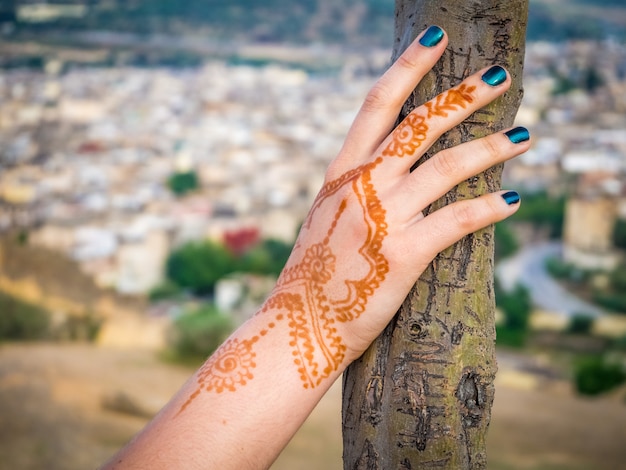 Free photo female's hand with a henna tattoo holding a tree with the beautiful cityscape