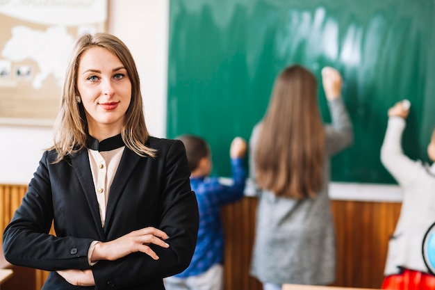 Female school teacher on background of blackboard and students