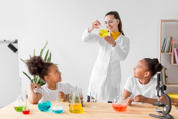 Female scientist teaching girls chemistry while holding tube with potion