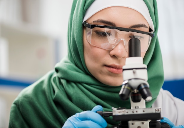 Female scientist with hijab looking through microscope