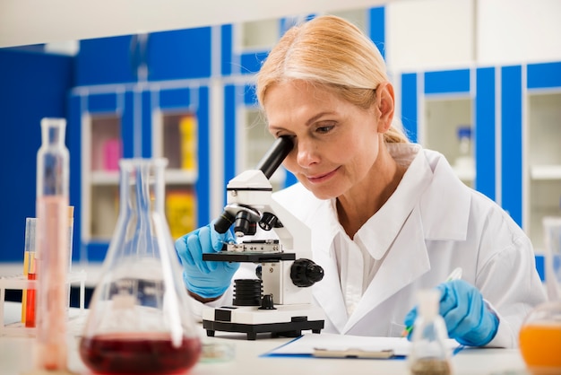 Free Photo female scientist with surgical gloves looking through microscope