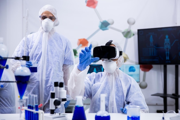 Female scientist working with virtual reality goggles in research laboratory with her assistant in the background.