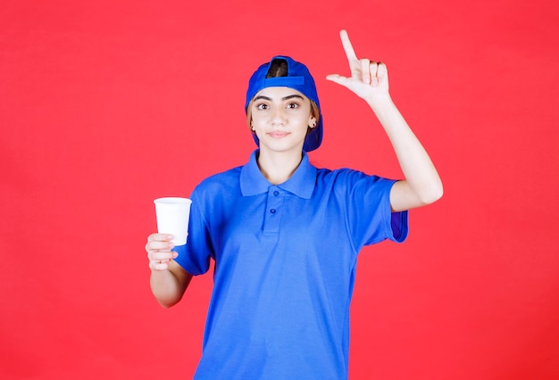 Free Photo female service agent in blue uniform holding a disposable cup of drink and having a good idea. 