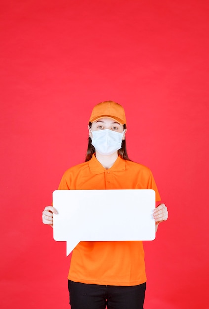 Free Photo female service agent in orange color dresscode and mask holding a white rectangle info board.