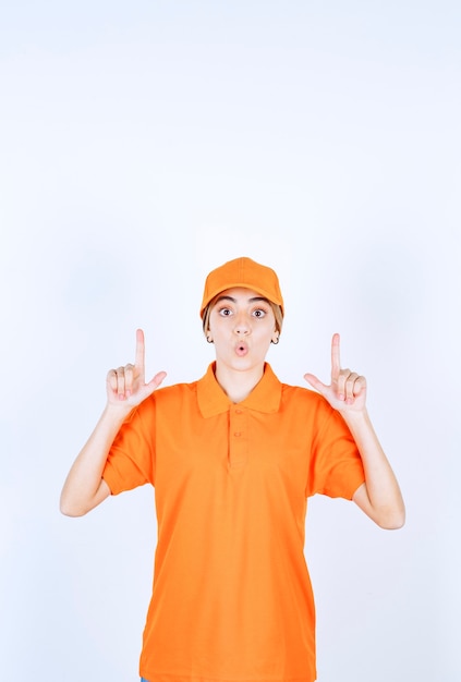 Free Photo female service agent in orange uniform pointing at something above with emotions