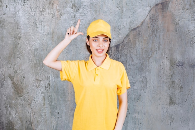 Free photo female service agent in yellow uniform standing on concrete wall and showing above.